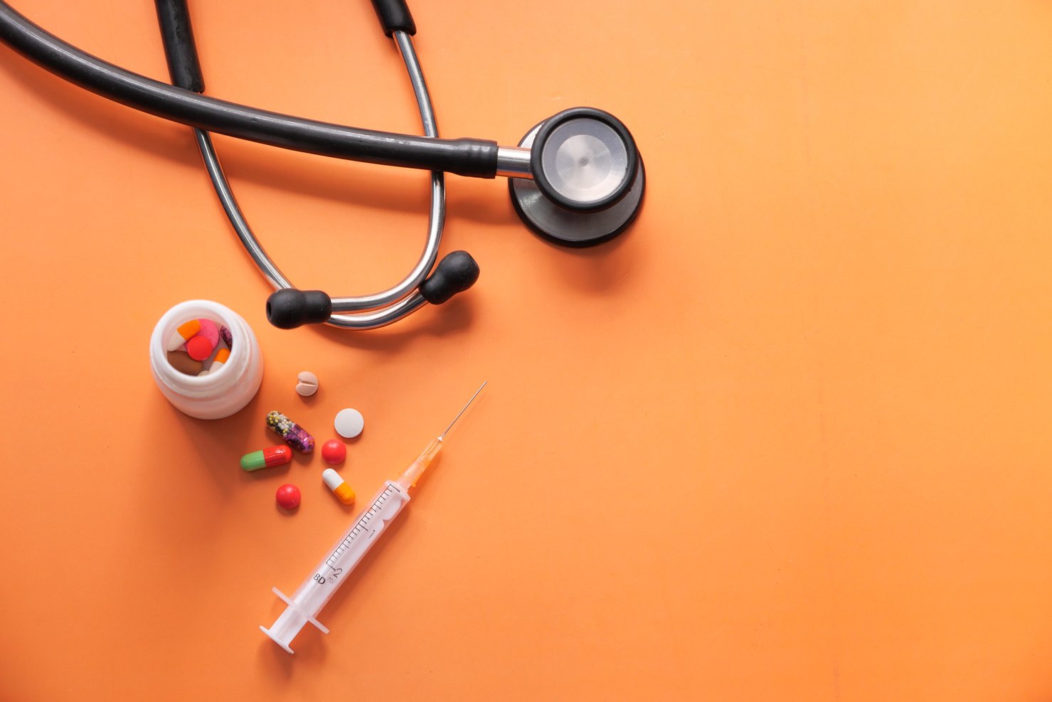 Top View of Stethoscope, Pills and Syringe on Orange Background